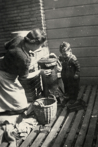 604412 Afbeelding van Peter van der Linden die zijn moeder helpt bij schoonmaken van de kolenkachel op het balkon van ...